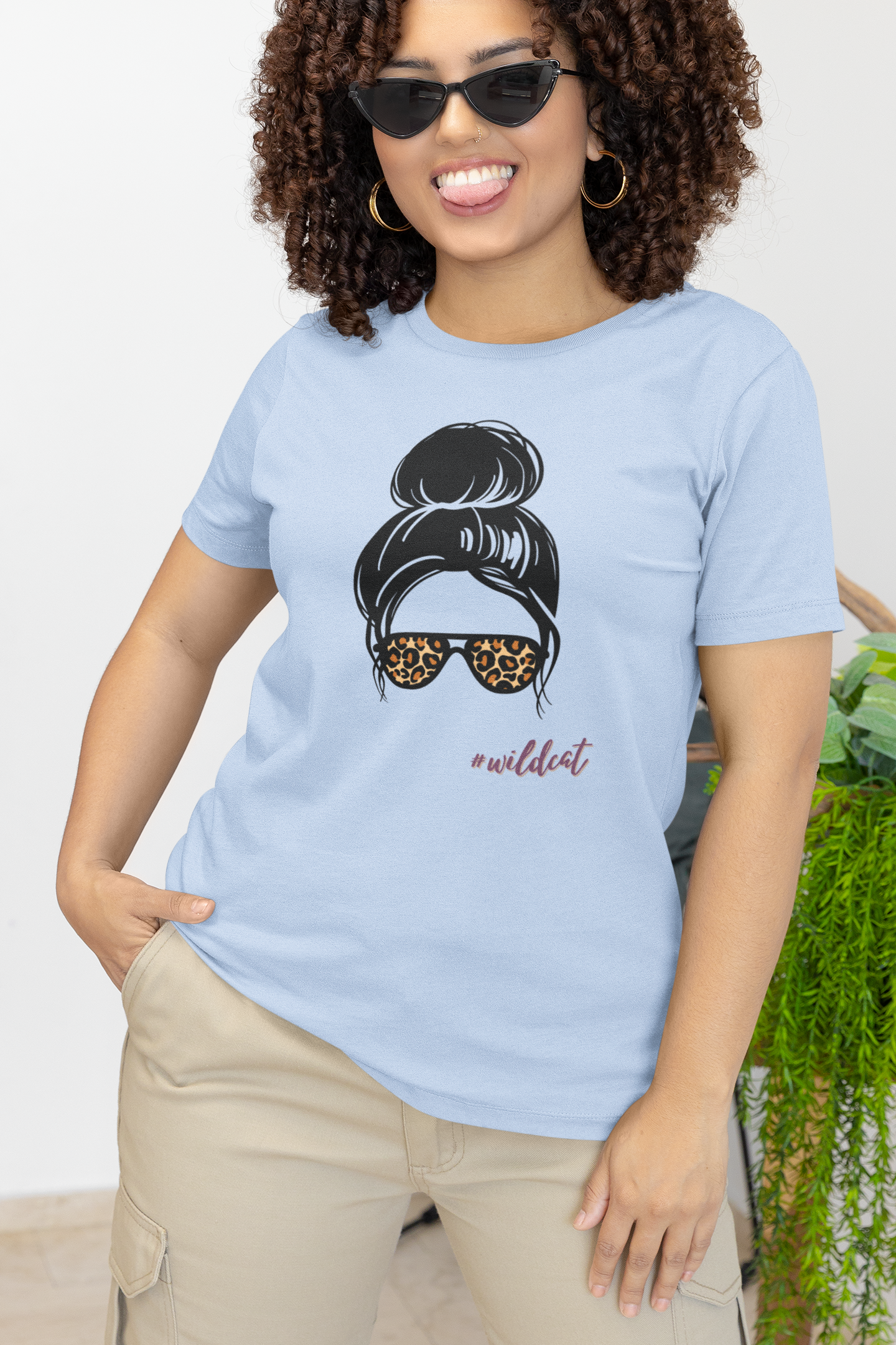 Woman wearing a light blue t-shirt with a graphic design and text, standing against a white background.