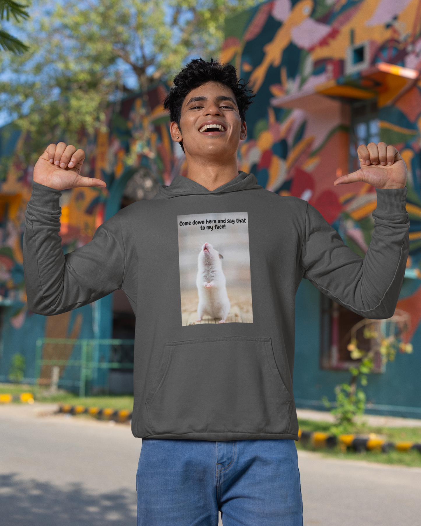 Person wearing a hoodie with a mouse graphic and text, standing in front of a colorful mural.