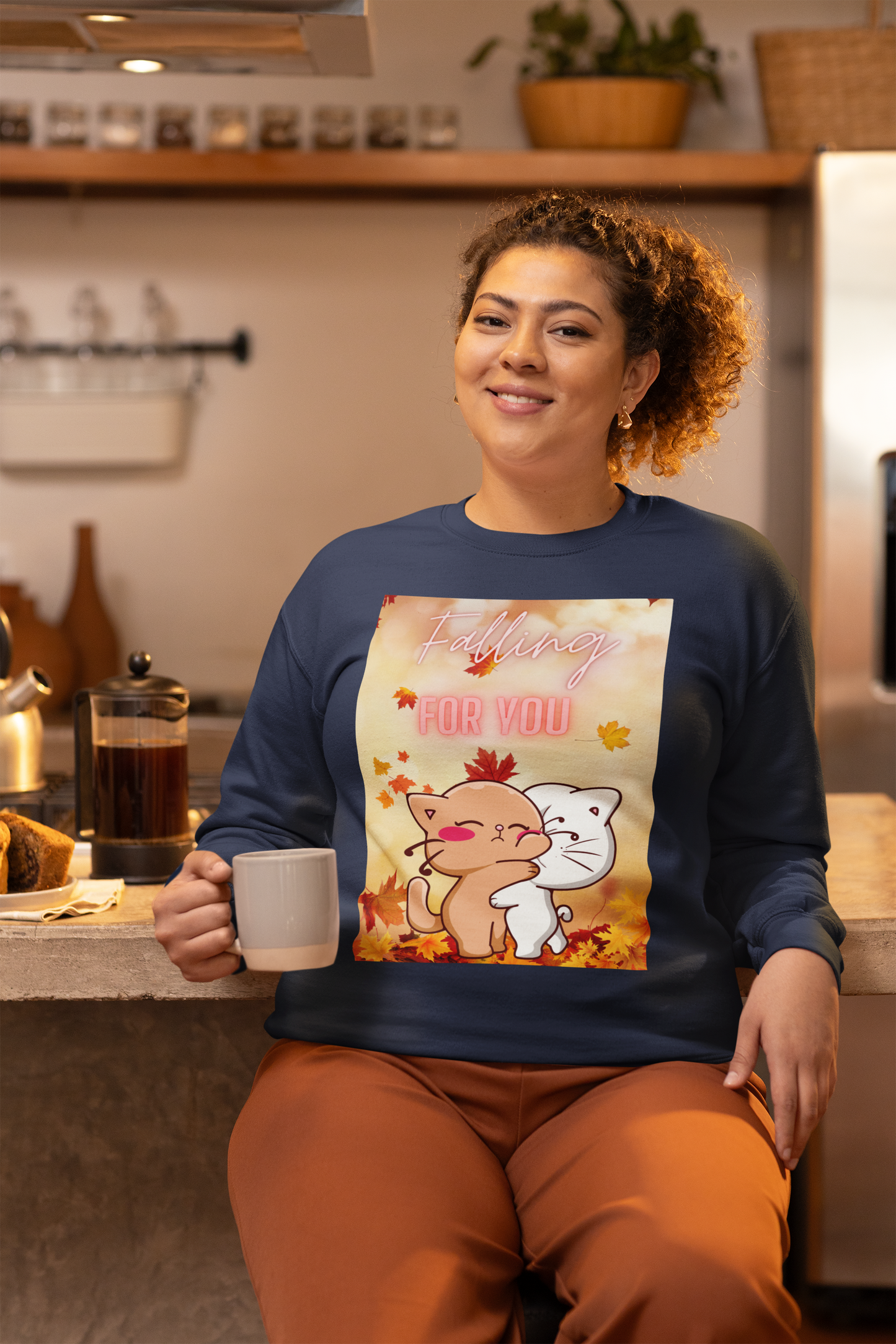 Woman in a kitchen wearing a sweater with a cartoon design, holding a mug.