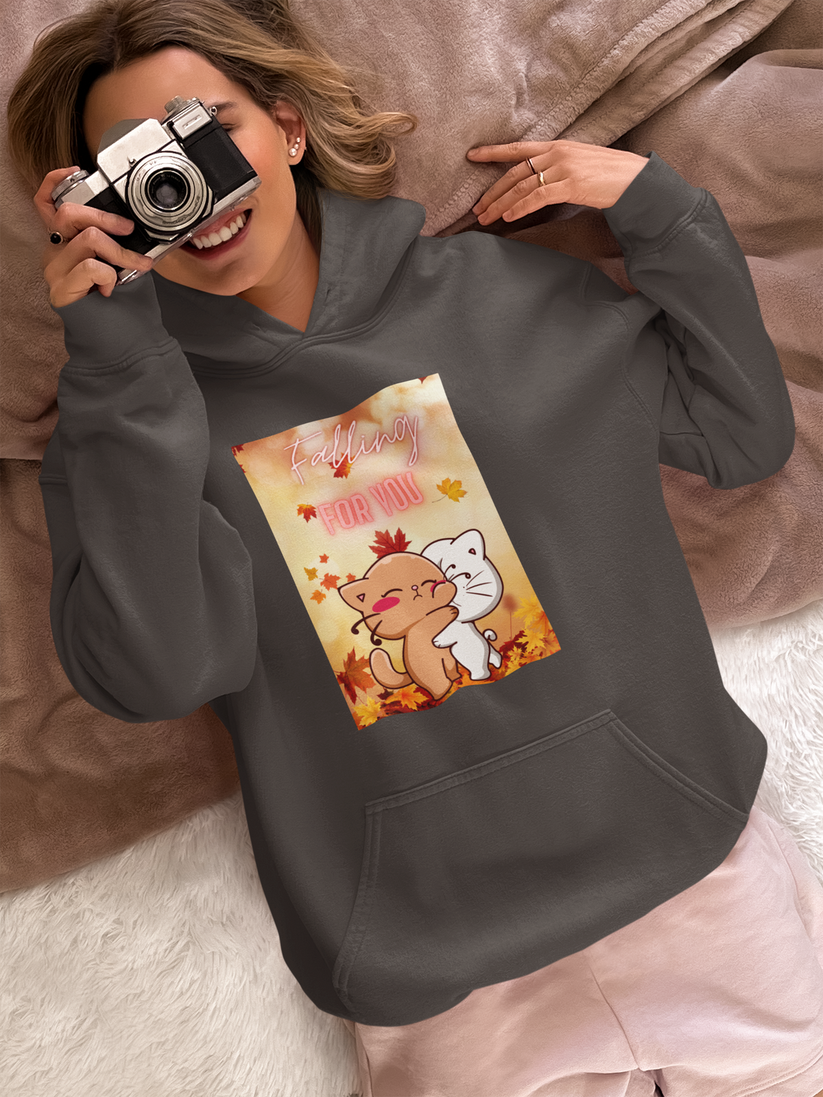 A person is wearing a hoodie featuring a cartoon design of two hugging cats holding a camera.